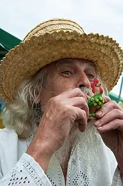 A man blowing into a small whistling toy shaped like a rooster