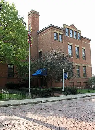 three story brown brick early 20th century school building with chimney and trees