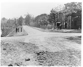 A grayscale view of a rural dirt road with a building visible to the right