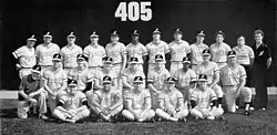 A black and white photograph of baseball players in uniforms and caps posed in three rows standing, sitting, and kneeing on a baseball field
