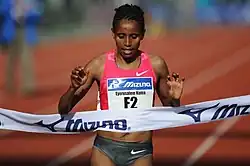 Photo of Eyerusalem Kuma running on tracks and reaching the finish line ribbon