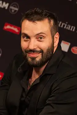 close-up of Václav Bárta wearing an open-necked black shirt and black blazer, smiling broadly at camera