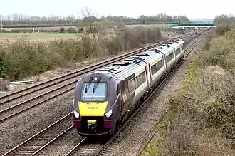 Engine with passenger carriages approacing on a left turn flanked by a stand of trees taken from an overbridge