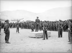 A military officer on a podium delivers a speech to gathered troops