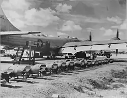 A black and white photograph of an aircraft with multiple bombs on its right side ready to be loaded