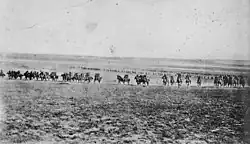 A line of men on horses charge across an open field towards the camera.