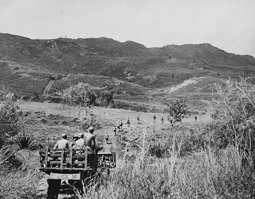 A marine tractor, loaded with ammunition and water, follows Marines along a road leading to the front lines
