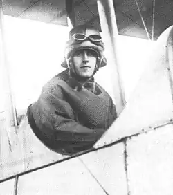 Half-portrait of man in flying helmet and goggles seated in the open cockpit of a biplane