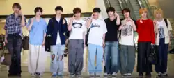 Nine members of AHOF stand in a row, posing for cameras before departure. They were casual outfits and gesture toward the camera.