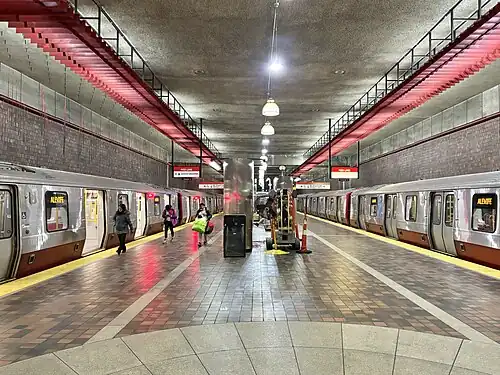 Two metro trains at an underground station platform with brick walls and floor