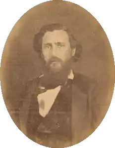 Sepia tone photo shows a bearded man in a black coat.