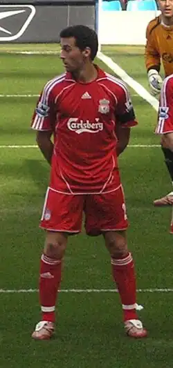 Man in red shirt standing with his arms behind his back.