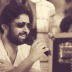 A photo of Aneesh Anwar smiling away from the camera holding a microphone.