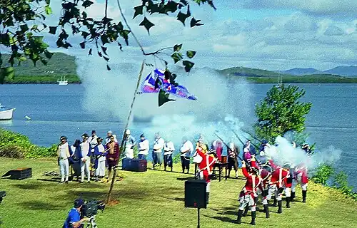 A group of about 12 people dressed in English military uniforms dating from around 1800, shooting their rifles into the air