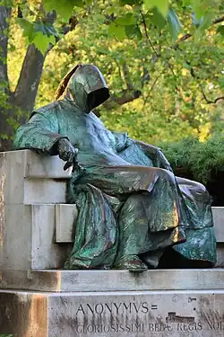 A man wearing a cowl which covers his face sits on a bench