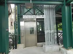 Green steel girders framing a steel sliding door with a window. Above it a sign reads "Elevator to Track 4, New York City, Ticket Machine, Street".