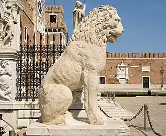 A large, light-colored marble statue of a lion standing on a plinth, with visible carvings on its body.