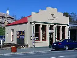A one-storey grey building with a large facade and a redish roof. A sign at the front reads Athenaeum.