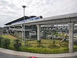 Wat Phra Sri Mahathat station (pictured in 2020, before the Pink Line station was built) now occupies the traffic circle's central island. The monument's last location, before its 2018 disappearance, is the lawn beyond the elevated rail tracks and the underpass.