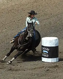 A woman on horseback makes a sharp turn around a white barrel.