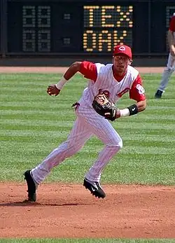 A man in a white baseball uniform with red pinstripes and a red baseball cap running to his left