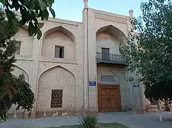 Early morning photo of a portion of the madrasa's cream-colored brick exterior, with light blue sky above