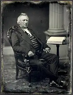 Daguerreotype of Bennet Tyler seated in an ornate chair beside a table with an open book, with a column in the background.