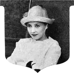 Black and white film still showing a woman in white dress and hat