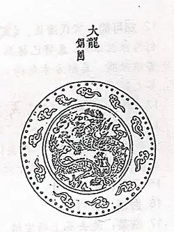 A drawing depicting a design inside of a circle, with that circle inside of a larger circle. The inner circle design contains a dragon curled in on itself, surrouned by flame. The outer circle contains a ring of small, isolated clouds spaced equally from each other.