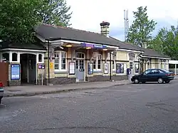 A yellow-brick building viewed from across the road with a car parked in front. A canopy hangs over part of the facade with a sign on it that says "Biggleswade". To the left of the building there is a gateway.