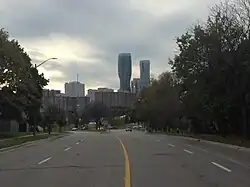 Looking down a wide four-lane road, divided into two lanes in each direction, towards the western terminus of Bloor St. with Mississauga City Centre beyond