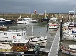 small boats lined up in harbour. Crane in the background & metal walkway in the foreground.