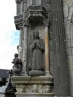 The kneeling Virgin Mary looks across to Gabriel. This sculpture is by Roland Doré. Around the vase containing lilies, is a banner reading "ECCE:ANCILLA:D(OMI)NI:FIAT:MIHI: SECVNDVM:VERBVM:TVVM"