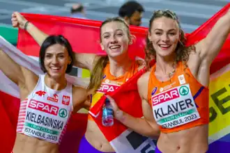 Photo of Anna Kiełbasińska holding a Polish flag behind her back and Femke Bol and Lieke Klaver each holding Dutch flags behind their backs, while posing for the camera