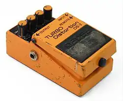 A small effect unit pedal, painted in orange paint that is scuffed from heavy use.