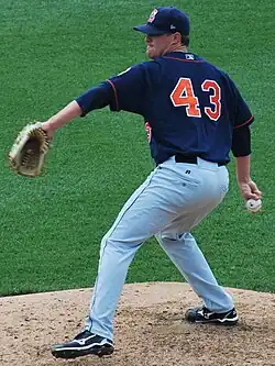 A man in a navy blue baseball uniform with "43" on the back rears back to deliver a pitch.