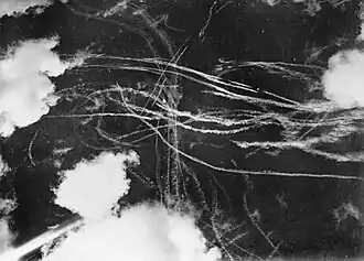 A picture of a piece of sky with several clouds and many condensation trails caused by many aircraft. Each trail curves around the other indicated an air battle