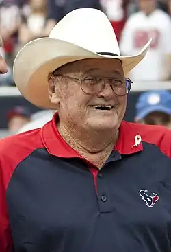 Photograph of a laughing Phillips wearing a Houston Texans polo shirt standing beside former U.S. President George H. W. Bush