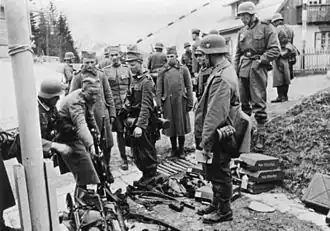 A black and white photograph of soldiers in helmets watching other soldiers laying down rifles in a pile