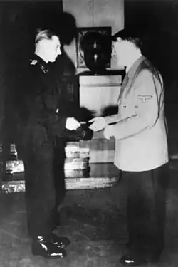 Wittmann, standing on the left, is shown receiving his Knight's Cross of the Iron Cross from Adolf Hitler standing on the right.