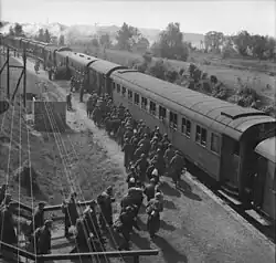 A black and white photo of numerous men, some carrying backpacks, heading for a train.