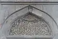 An intricately carved marble tympanum above an exterior window of the mosque
