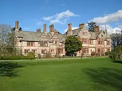 a country house of limestone and red sandstone, viewed across a lawn