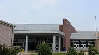 Front entrance to school with multiple exterior materials including red brick, ping brick, metal paneling, and windows