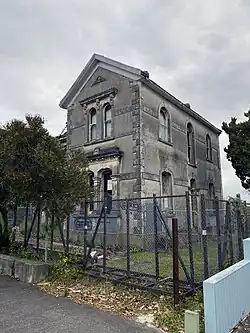 A side view of the Carlile House, a derilct building baracaded with a fence surronfing the perimeter of the property.