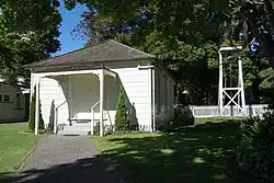 A view of a white chapel and an observation tower in a lush area