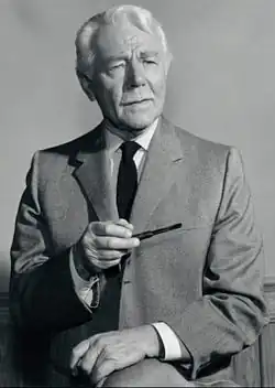 A black-and-white photograph of a man in a suit and tie with white hair and a pipe