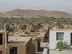 View looking out across Chupanan showing many adobe buildings and distant hills. Mostly tan spotted with dusty green trees.