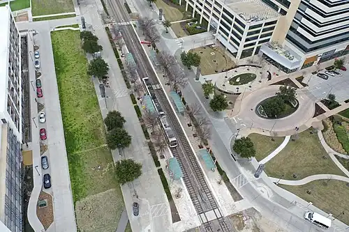 An aerial view of a double-tracked rail line surrounded by two side platforms. The CityLine development is visible to the right.