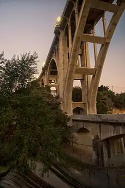 The Colorado Street Bridge 2020; view at sunset from underneath, showing hiking trail and lights on top of bridge.